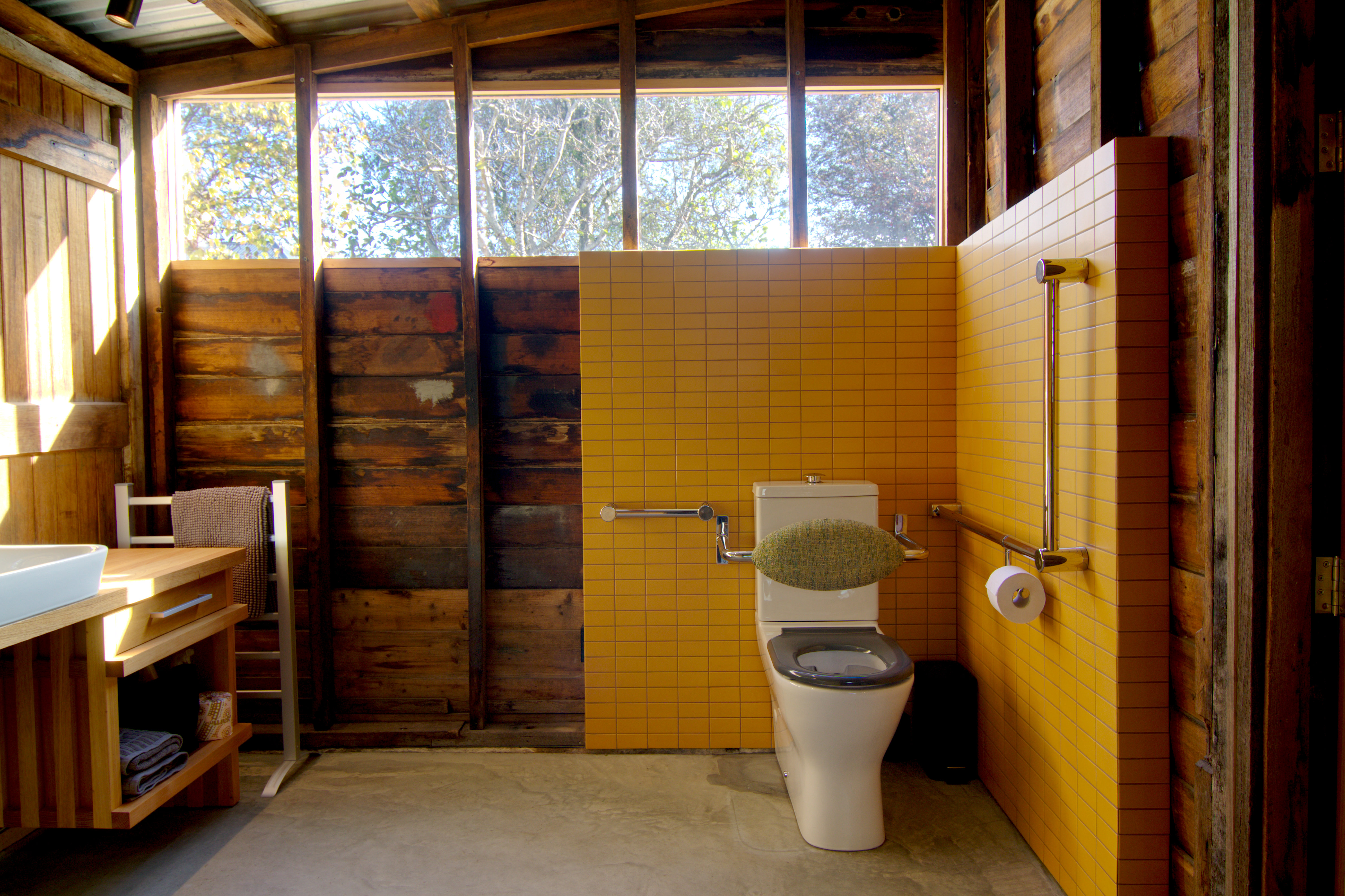 high window above toilet with grabrails on yellow tiled wall