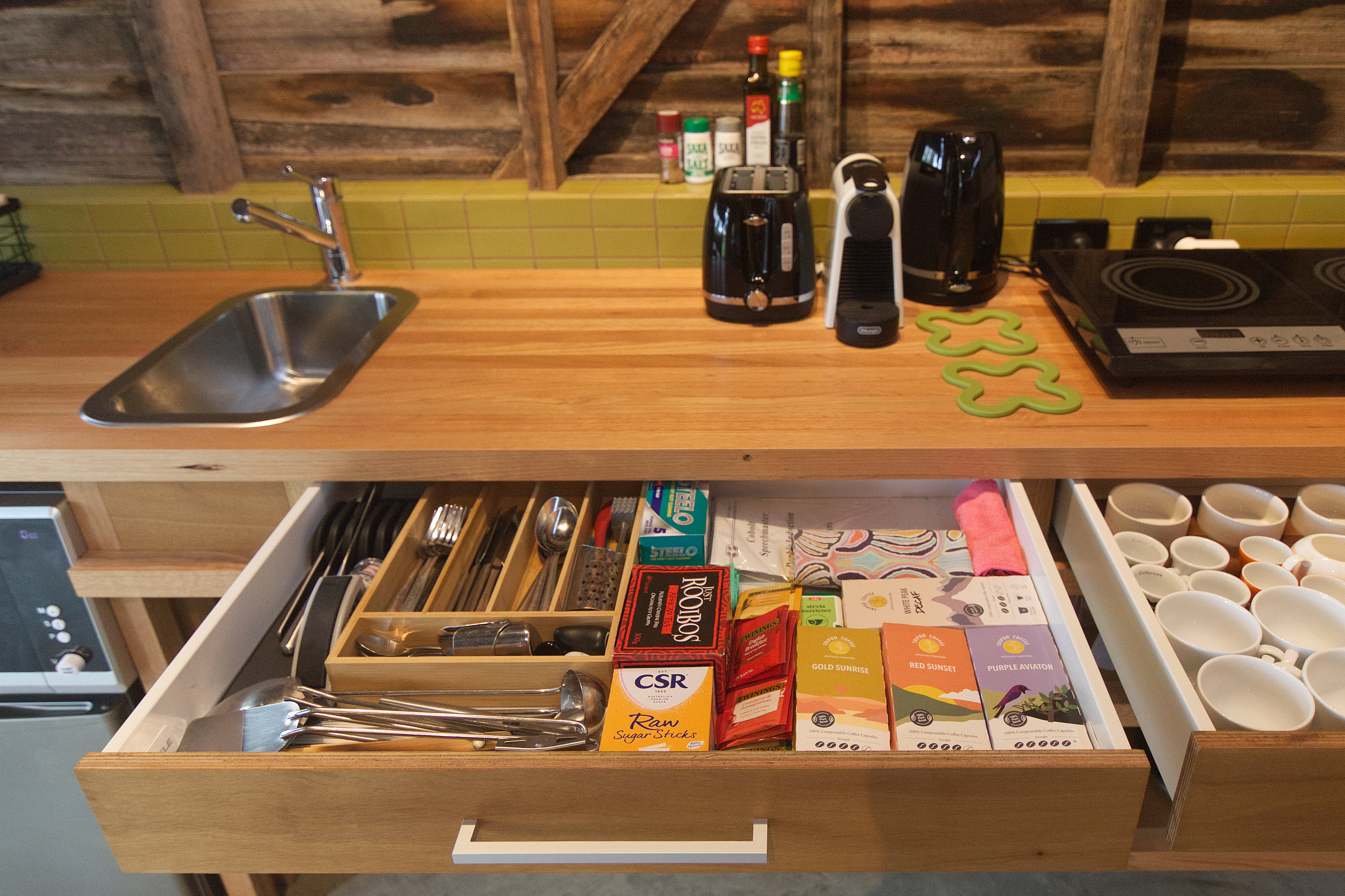 timber bench with sink, toaster, kettle, coffee machine and open drawer with coffee, tea and utensils