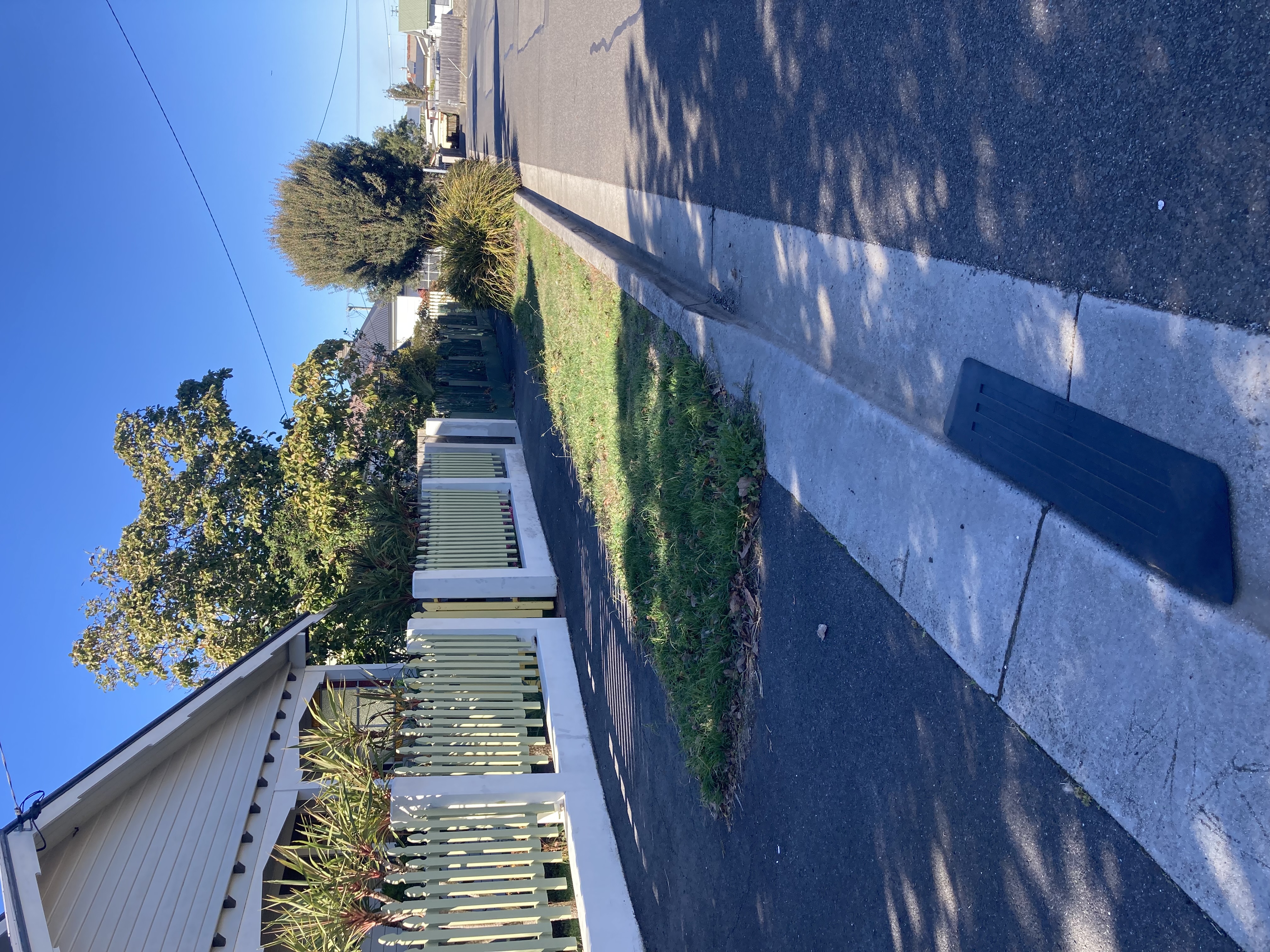 asphalt road, driveway and footpath in front of house with picket fence.