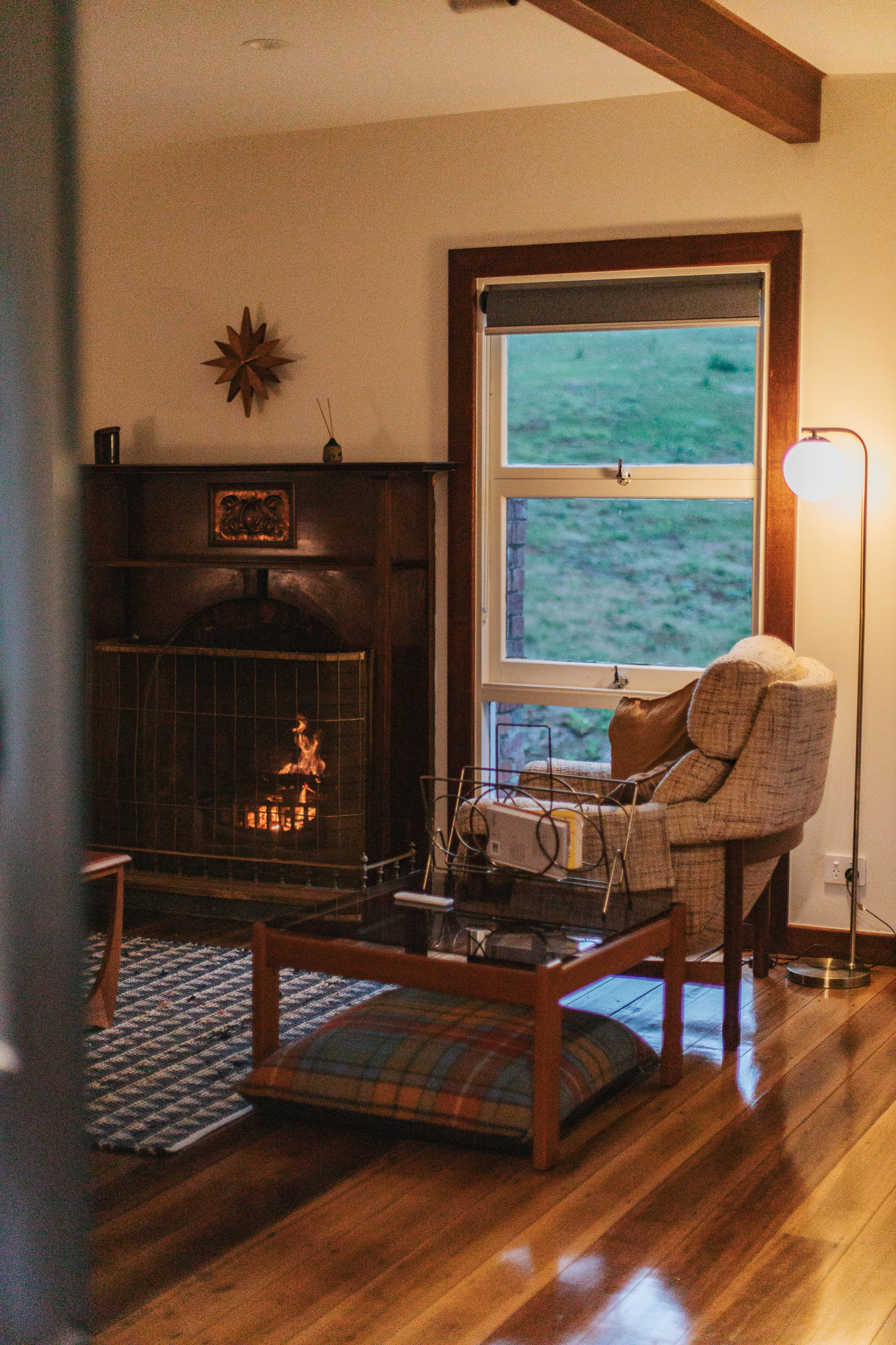 Indoor fireplace and armchair under warm lamp light.