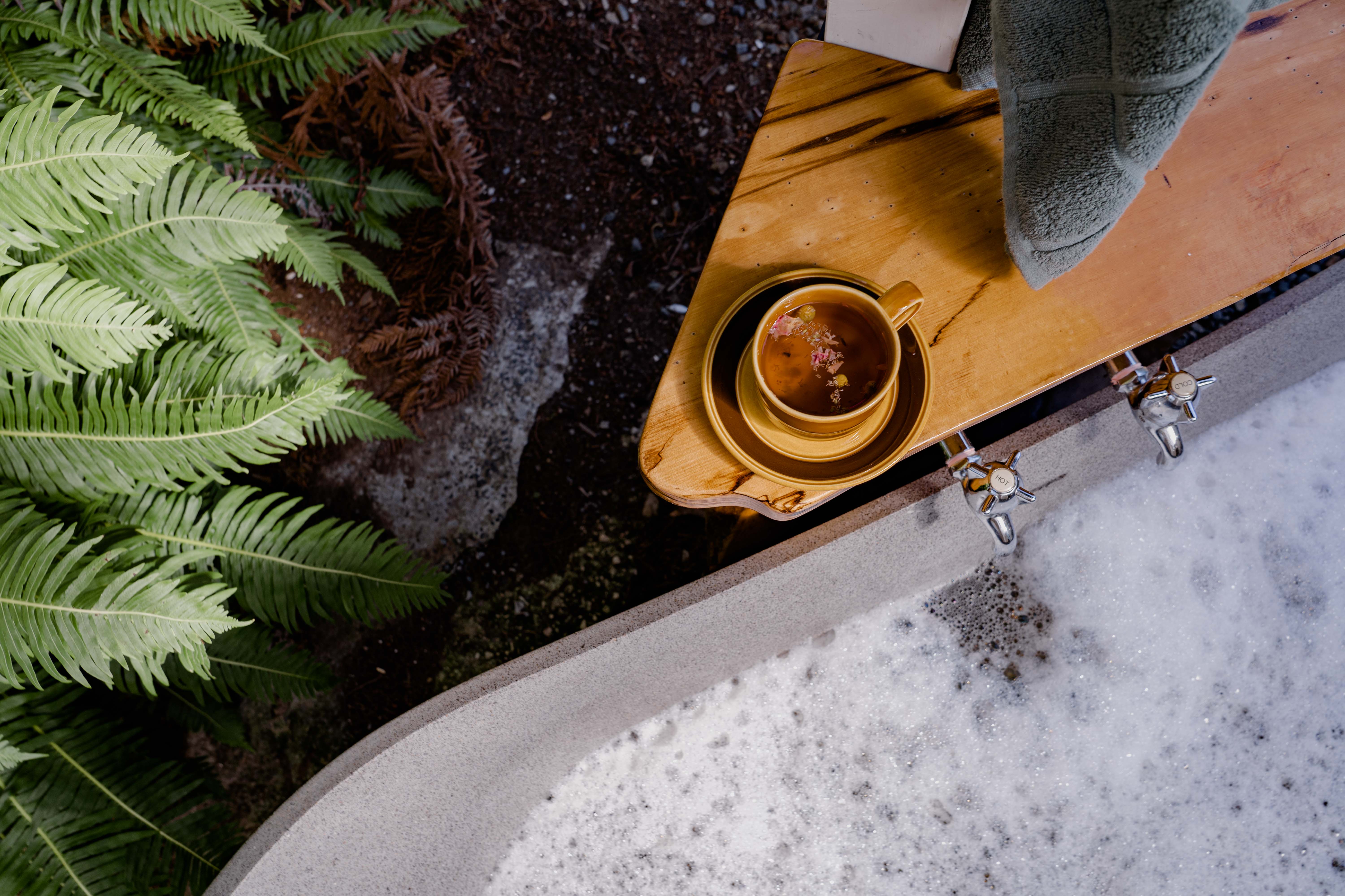 Birds eye view of outdoor bath and a cup of tea on the bath ledge.