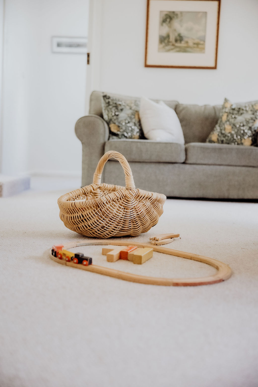 A wooden trainset and cane basket set up for children to play in a warm inviting living room.